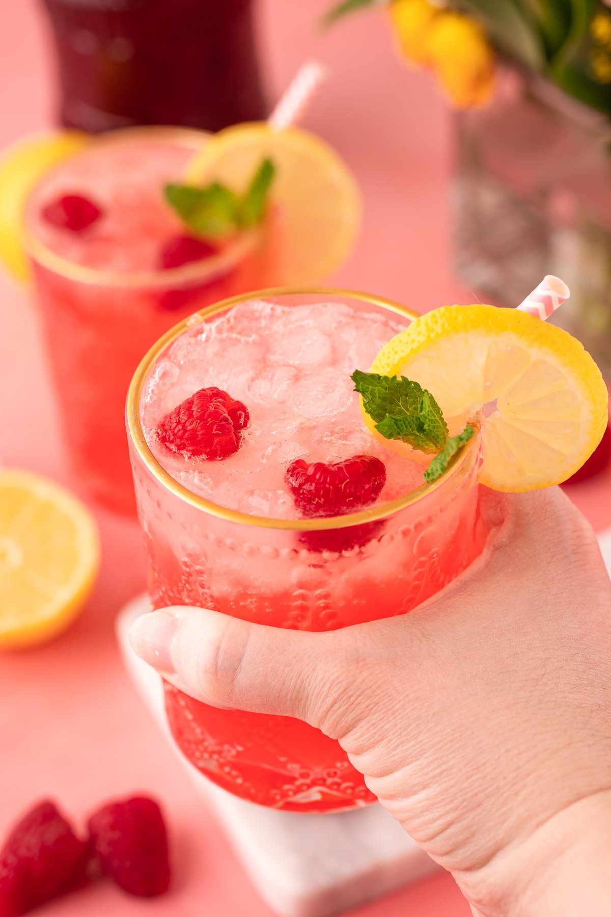 Woman's hand holding a raspberry gin daisy to the camera.