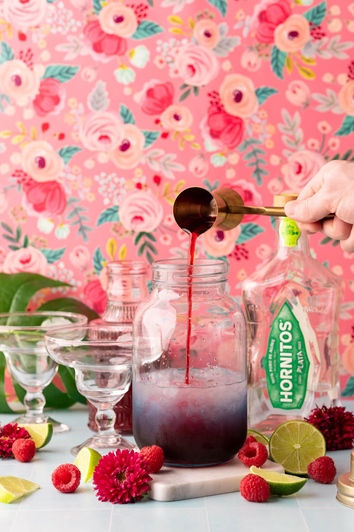 A jigger pouring raspberry simple syrup into a cocktail shaker.