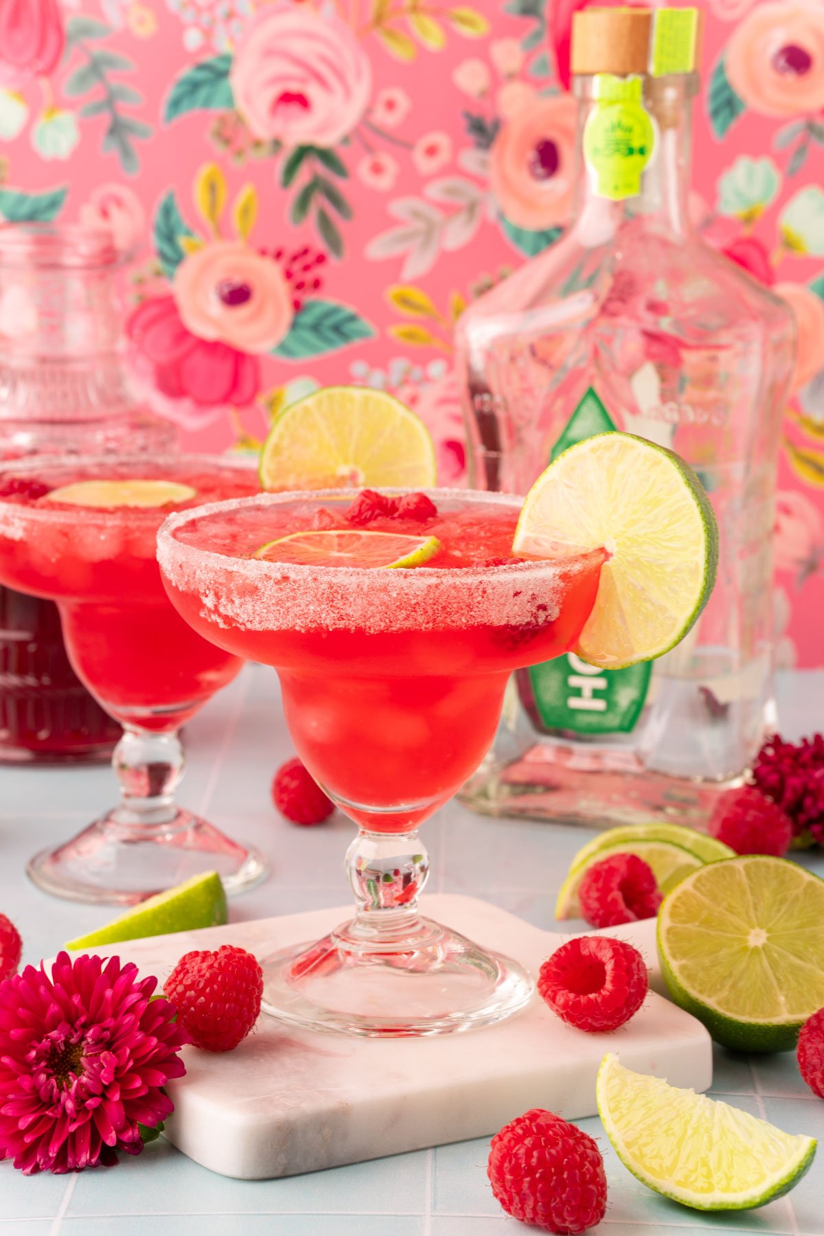 Two margarita glasses filled with raspberry margaritas on a blue table.