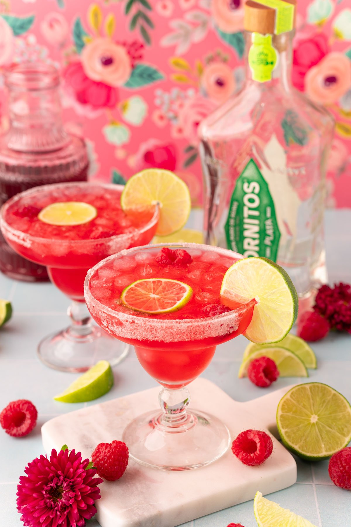 Two margarita glasses filled with raspberry margaritas on a blue table.