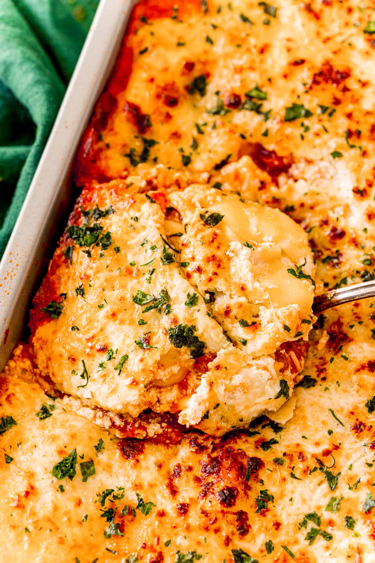 A spatula scooping a serving of ravioli lasagna out of a pan.