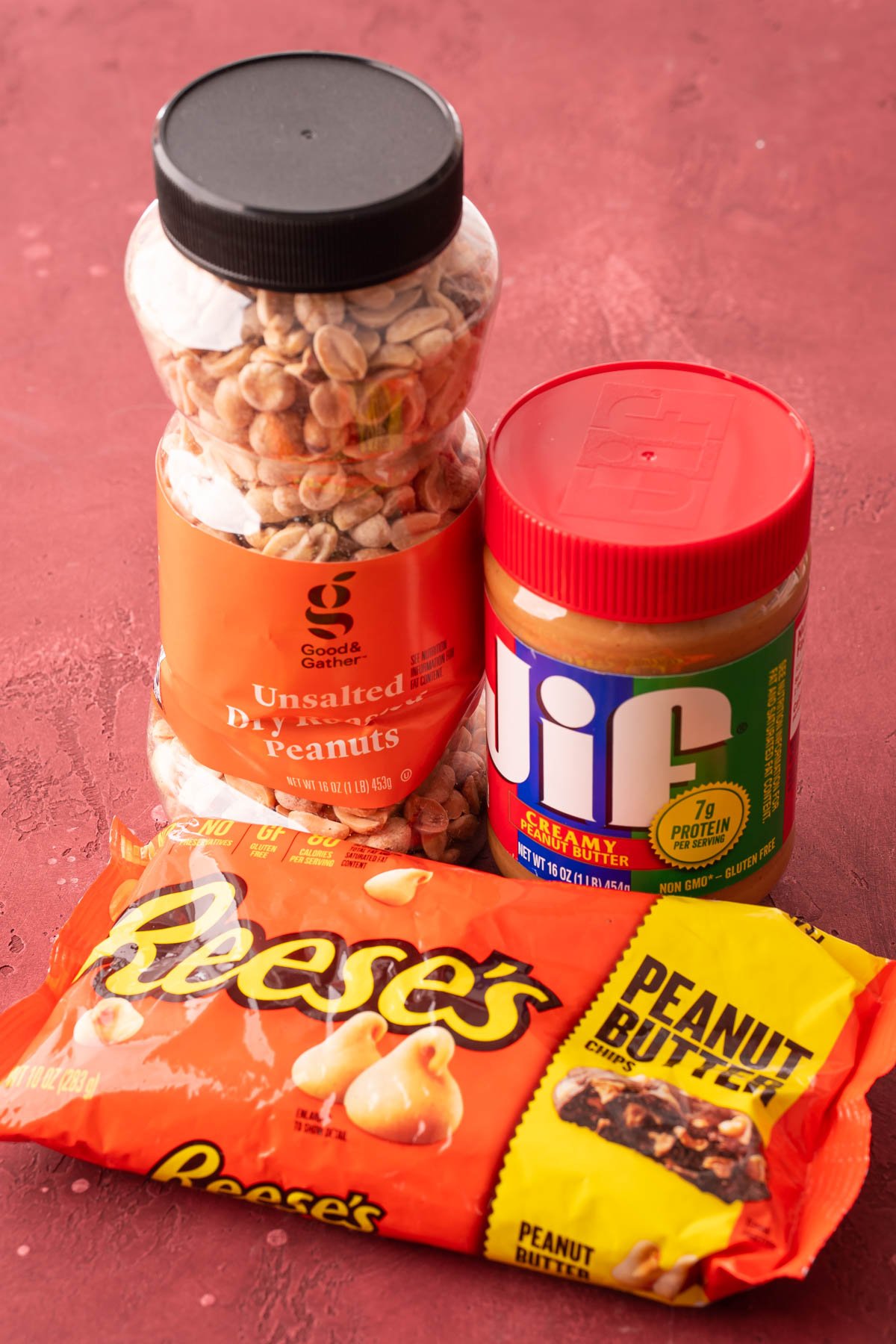 A container of peanuts, peanut butter, and a bag of peanut butter chips on a table.