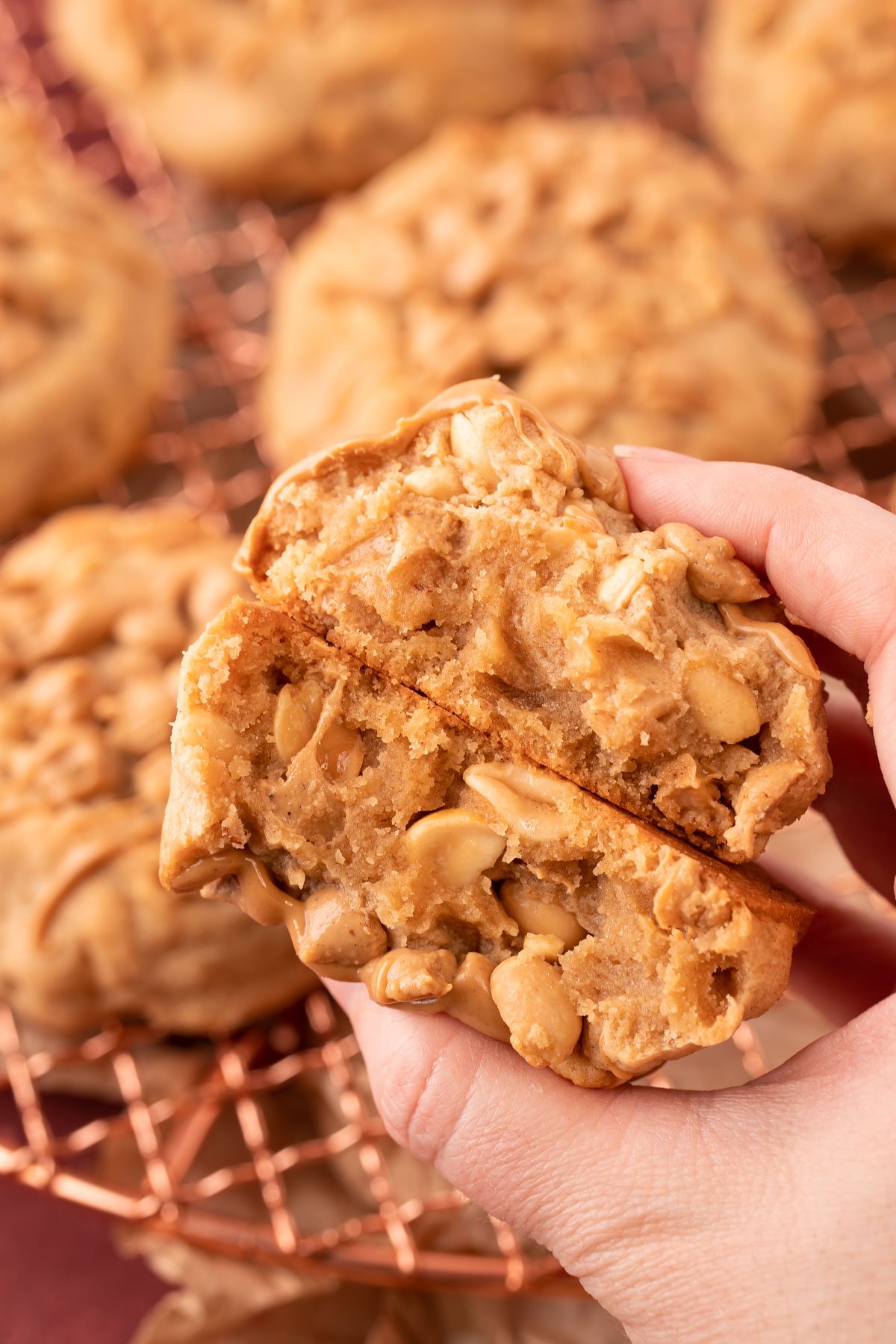 A woman's hand holding two halves of a triple peanut butter cookie to reveal the inside.