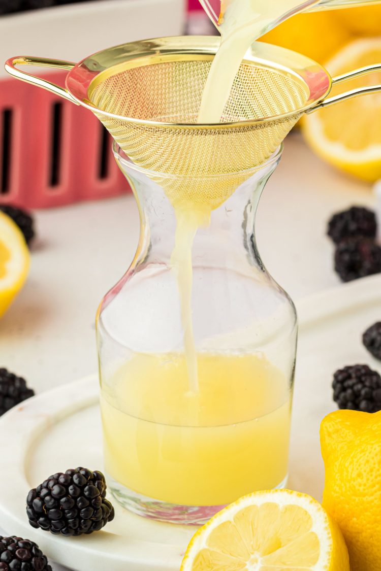 Lemon juice being poured through a fine mesh sieve into a bottle.