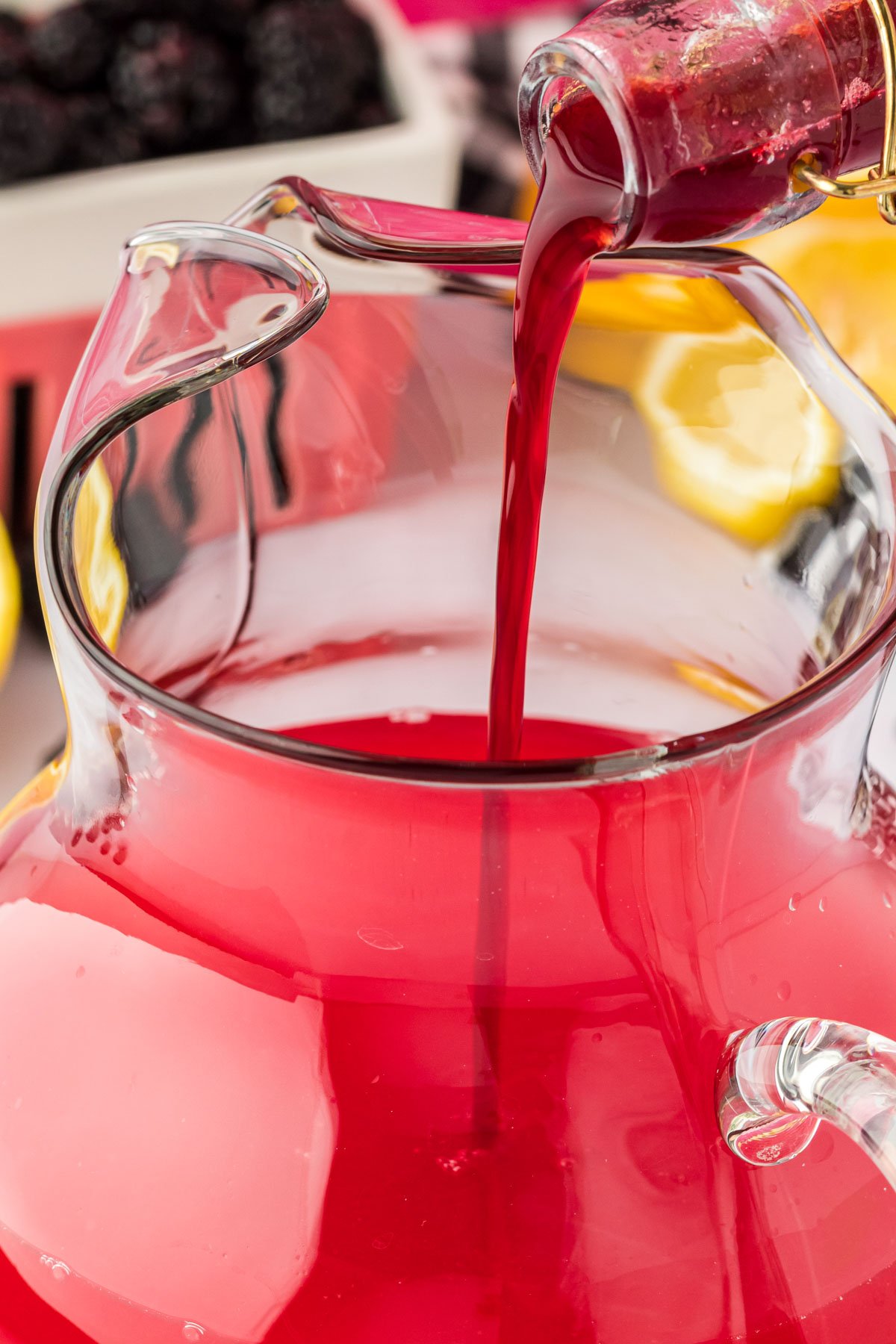 Blackberry simple syrup being poured into a glass pitcher to make lemonade.