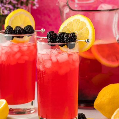 Two glasses of blackberry lemonade on a counter.