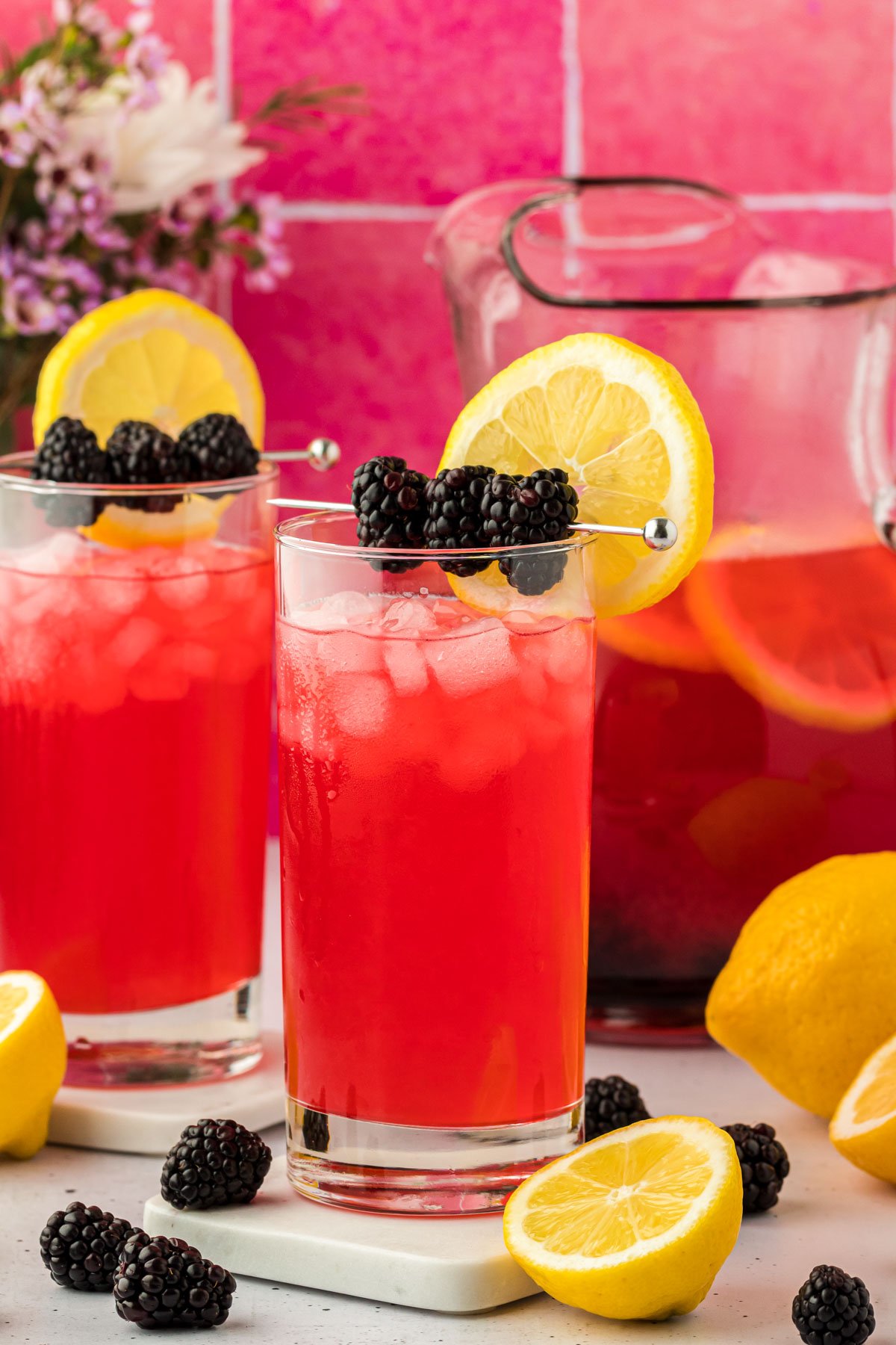 Two glasses of blackberry lemonade on a counter.