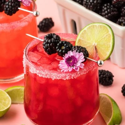 Blackberry Margarita garnished with blackberries, lime, and a flower on a pink surface.
