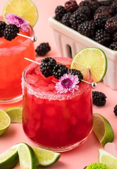Blackberry Margarita garnished with blackberries, lime, and a flower on a pink surface.