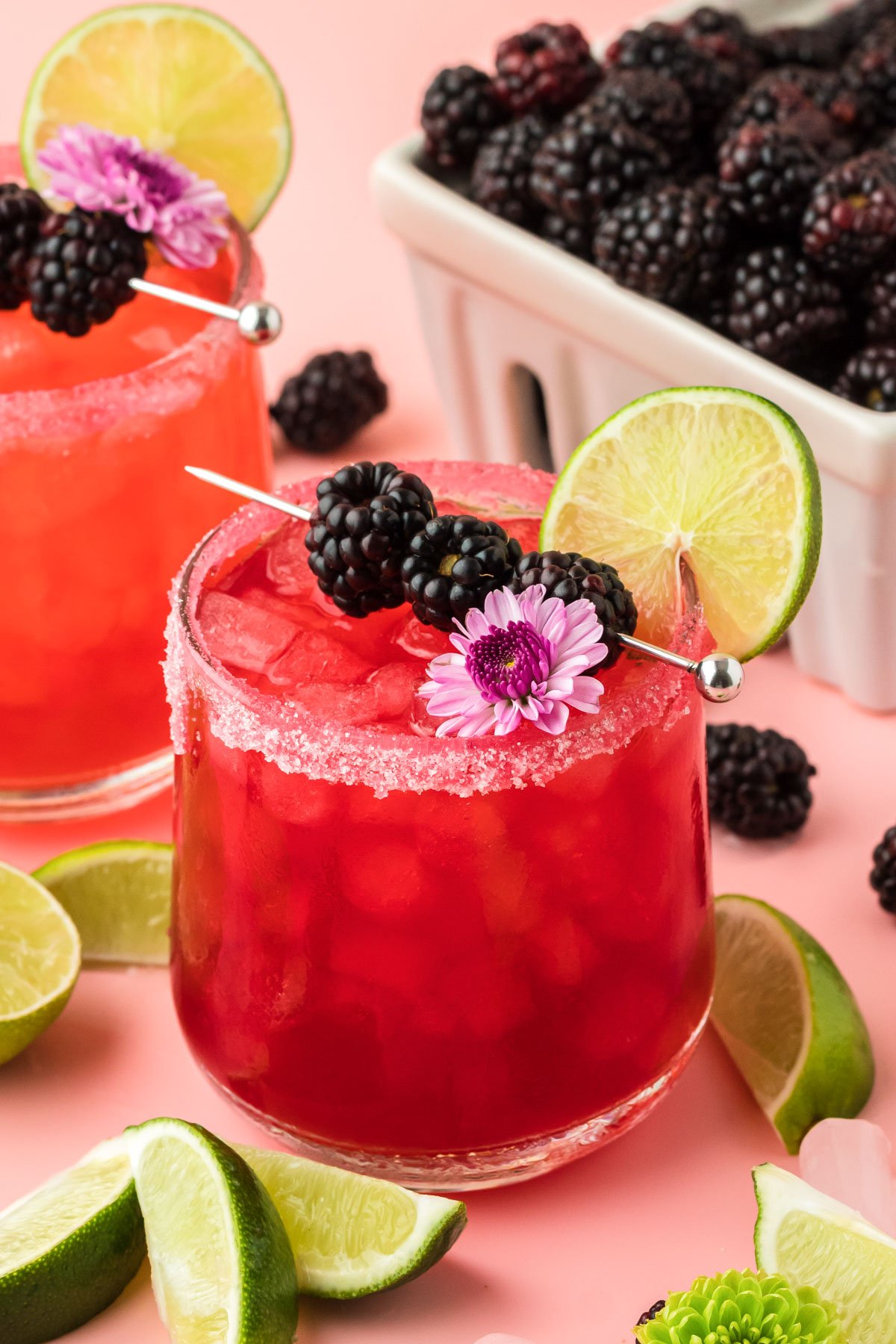 Blackberry Margarita garnished with blackberries, lime, and a flower on a pink surface.