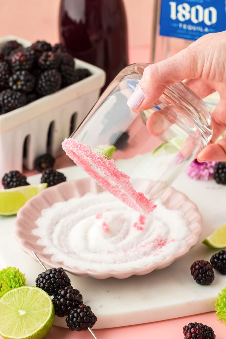 The rim of a glass being dipped in a plate of sugar to make a sugar rim for a margarita.