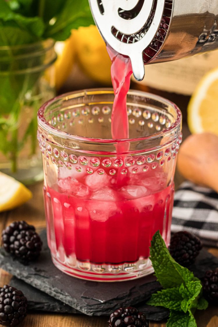 A blackberry bourbon smash being poured into a glass from a cocktail shaker.