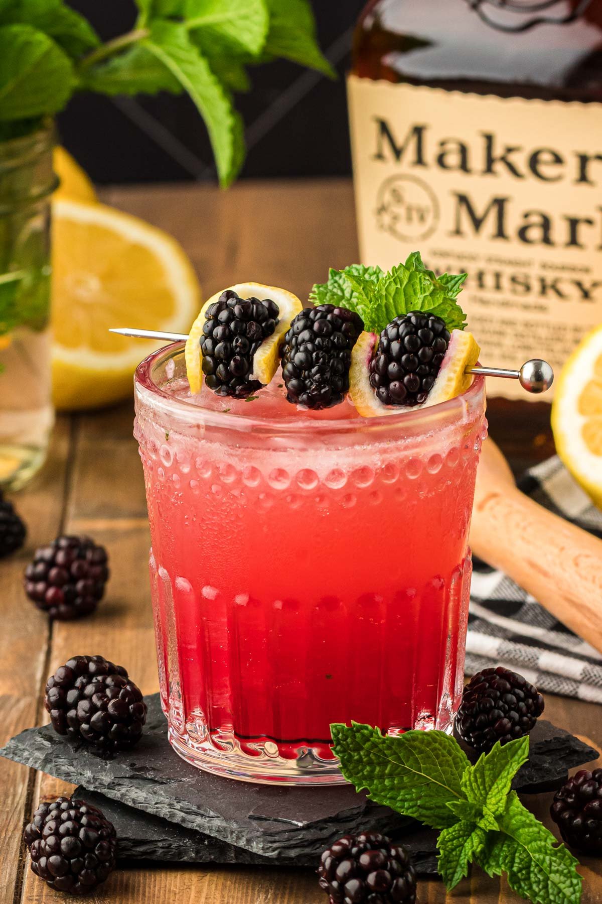 A glass with a bourbon smash (blackberry flavored) on a black coaster.