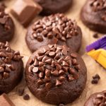 Caramel stuffed chocolate cookies topped with mini chocolate chip on parchment paper.