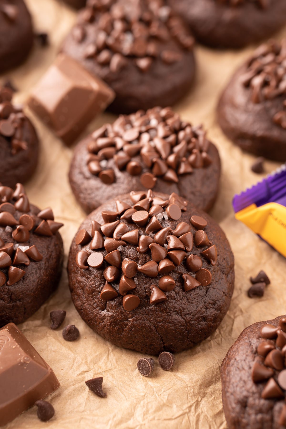 Caramel stuffed chocolate cookies topped with mini chocolate chip on parchment paper.