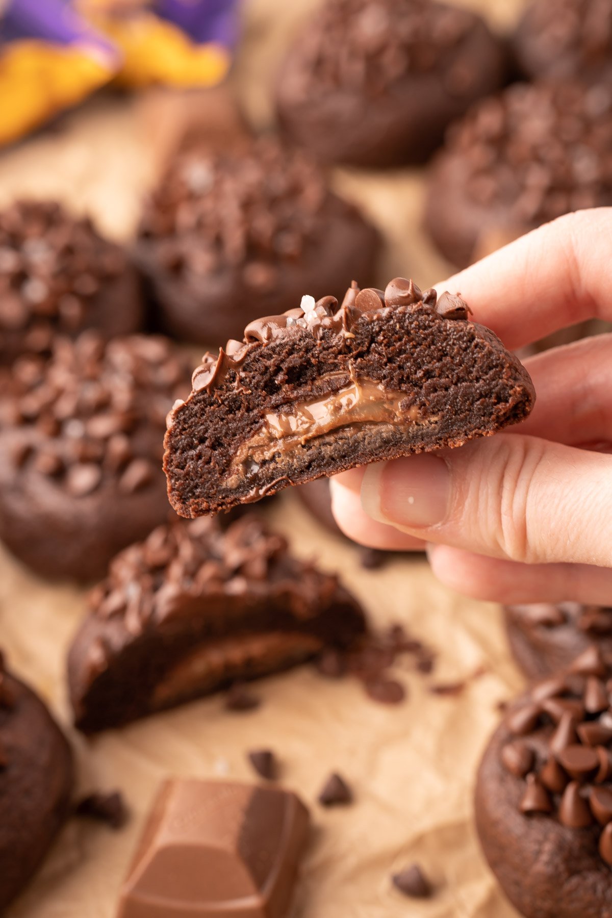 A woman's hand holding a chocolate cookie stuffed with caramel to the carmera.