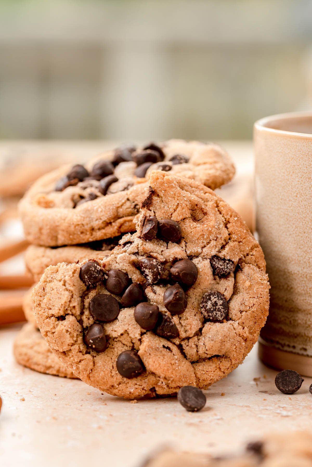 A stack of cinnamon chocolate chip cookies with one with a bite missing resting on the stack near a mug.