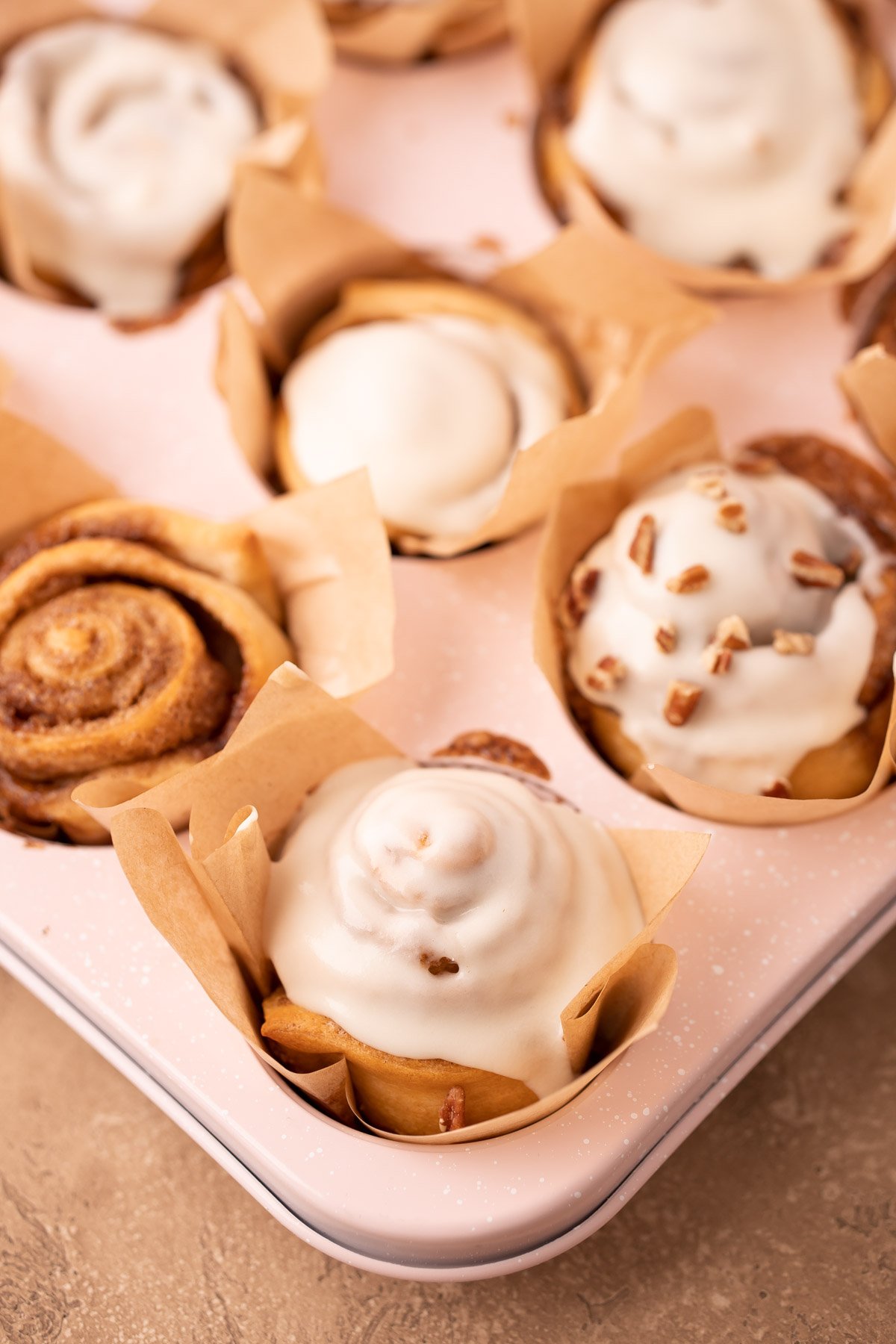 Cinnamon roll muffins in a muffin tin, some have been topped with icing.