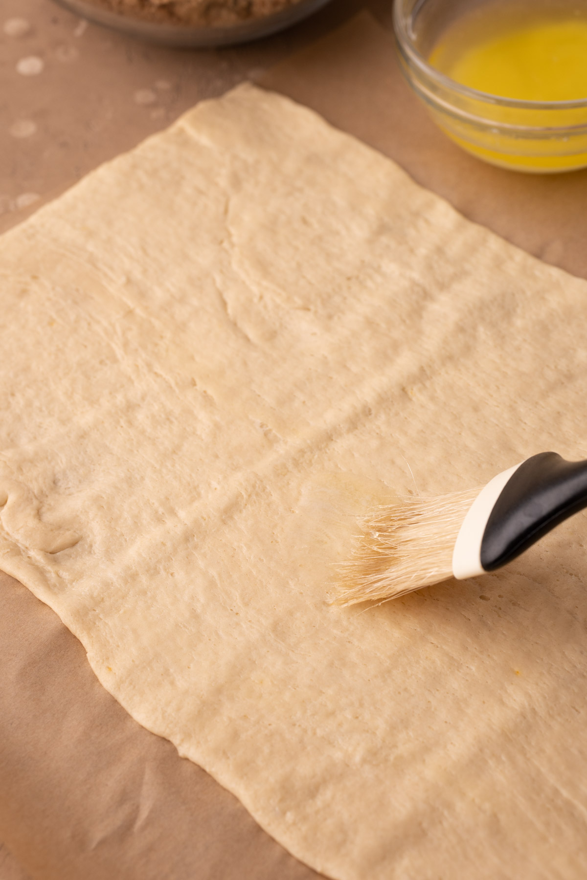 A pastry brush brushing a crescent roll dough sheet with melted butter.