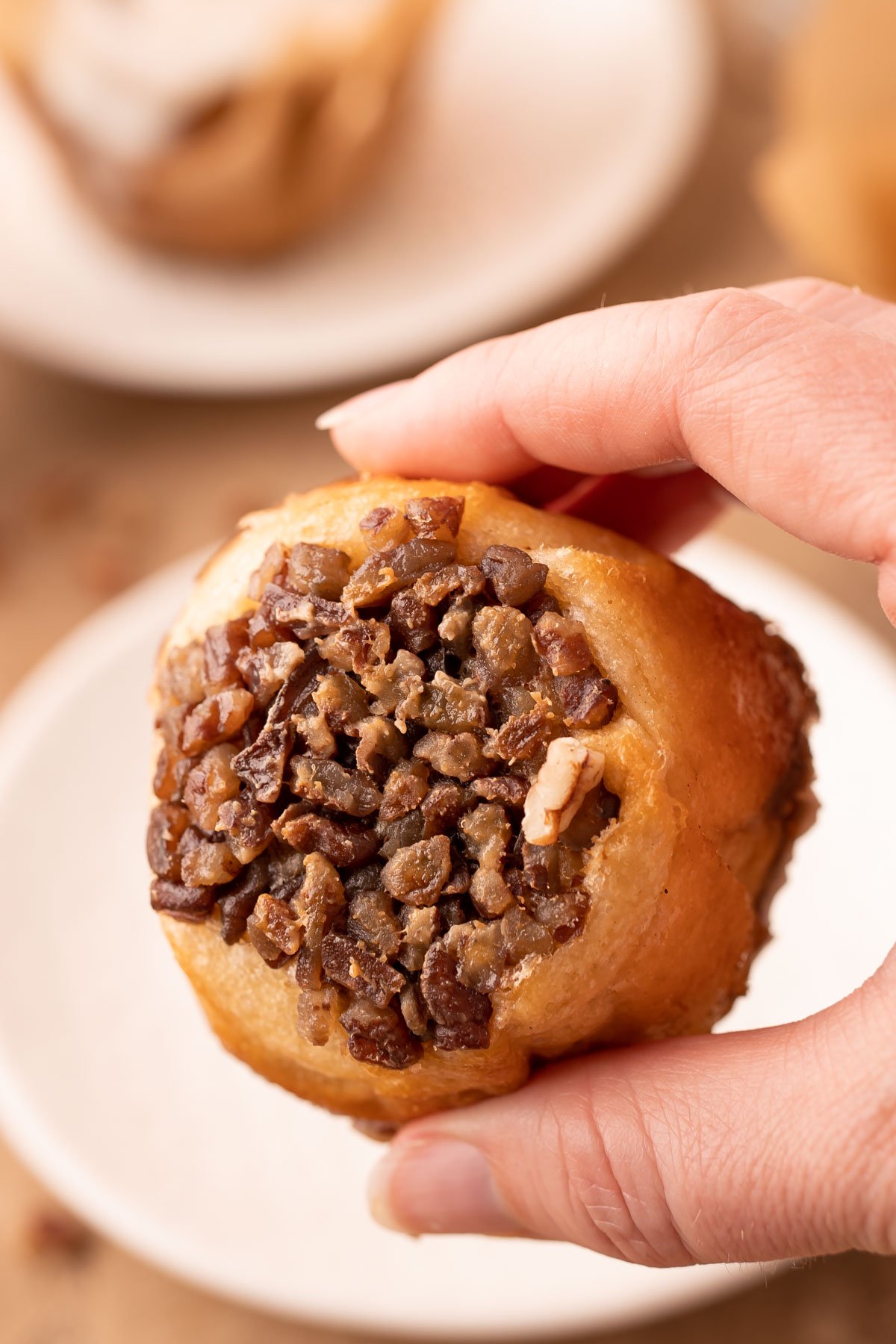 A woman's hand holding a pecan roll muffin showing the bottom. 