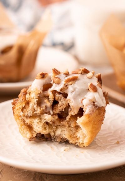 A crescent roll cinnamon pecan roll muffin on a white plate with a bite missing.
