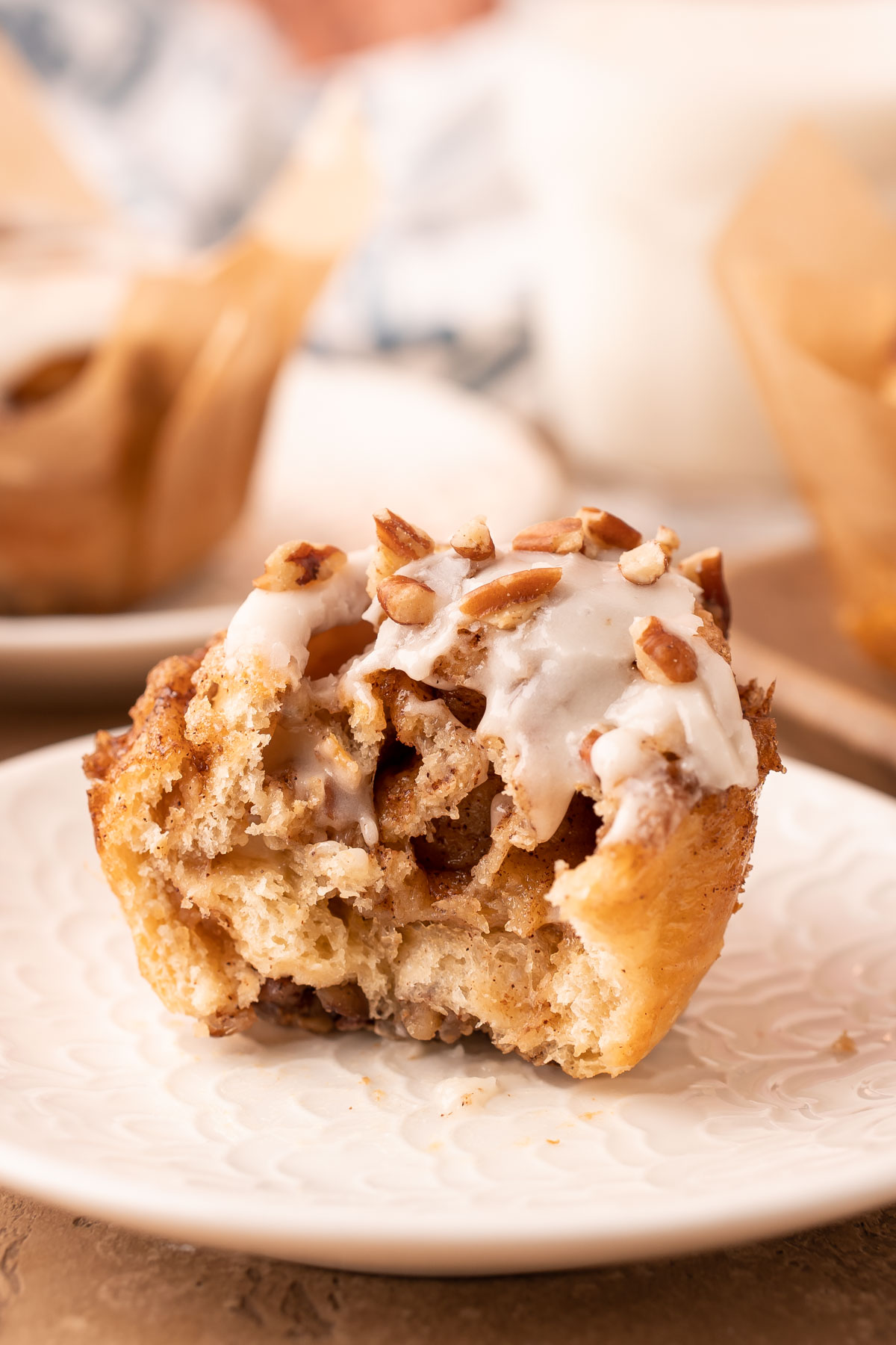 A crescent roll cinnamon pecan roll muffin on a white plate with a bite missing.
