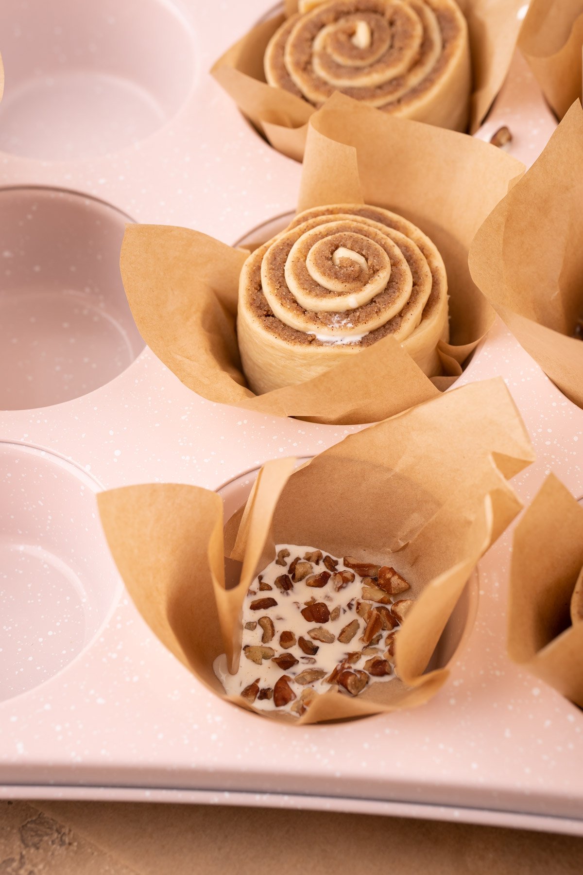 A muffin tin being filled with liners to make cinnamon rolls.