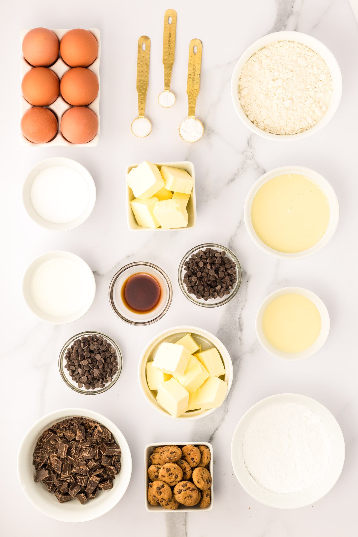 Ingredients to make milk and cookies cupcakes prepped on a marble counter.