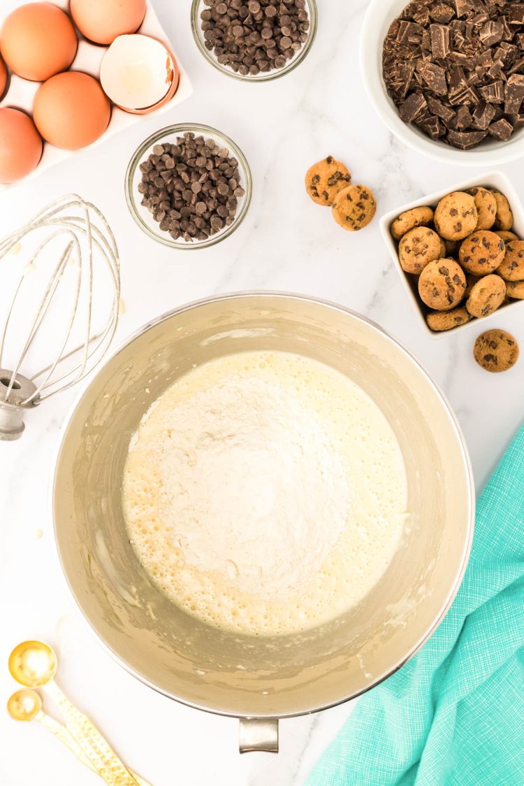 Flour being added to a stand mixer bowl with batter to make cupcakes.