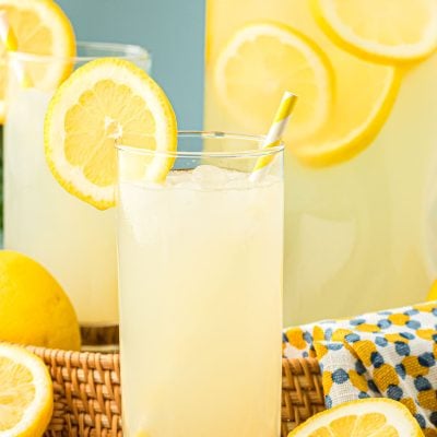 Homemade Lemonade in a glass with a pitcher behind it.