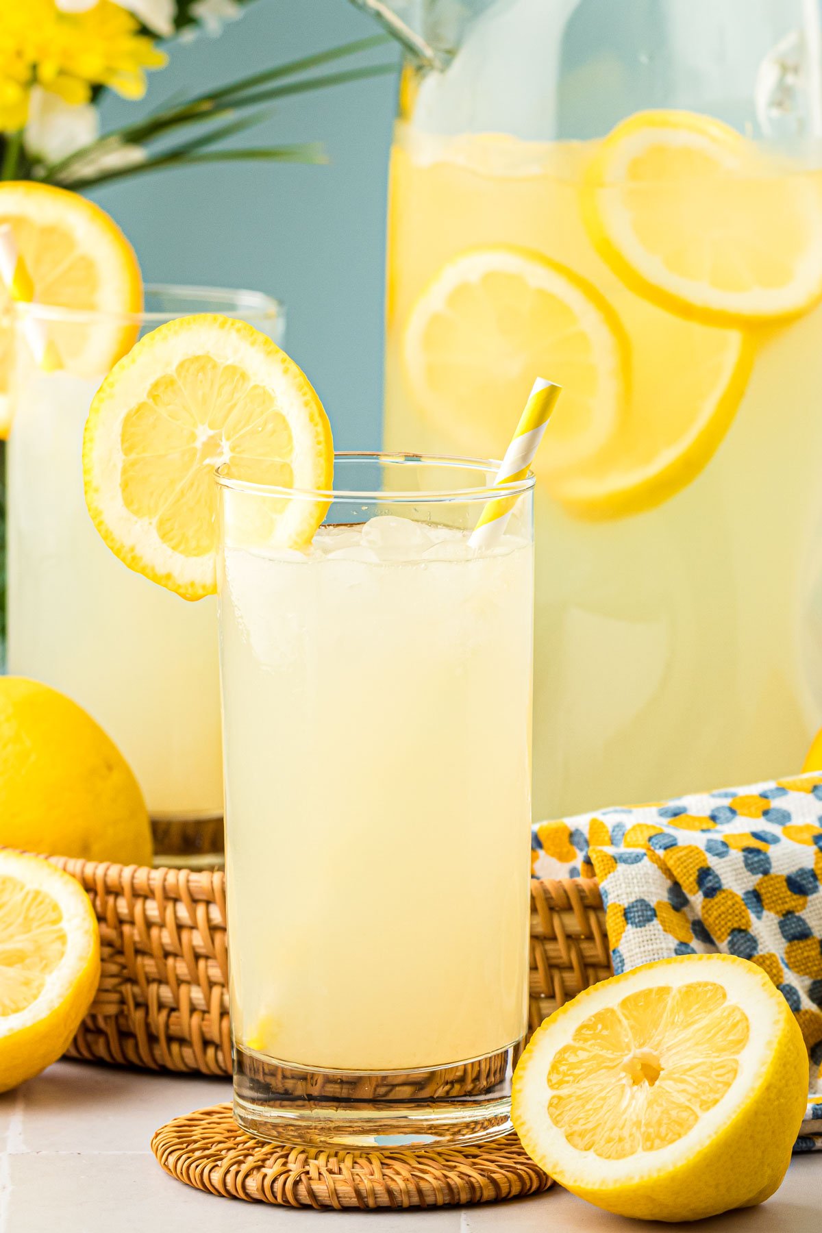 Homemade Lemonade in a glass with a pitcher behind it.