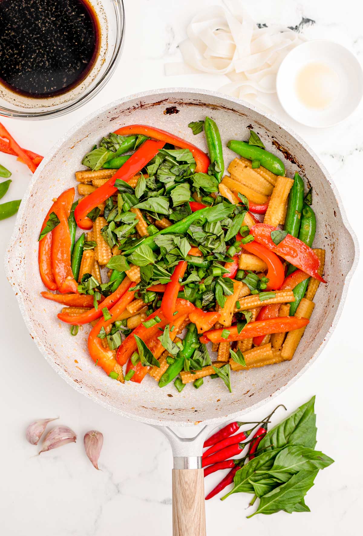 Herbs being added to a skillet with veggies.