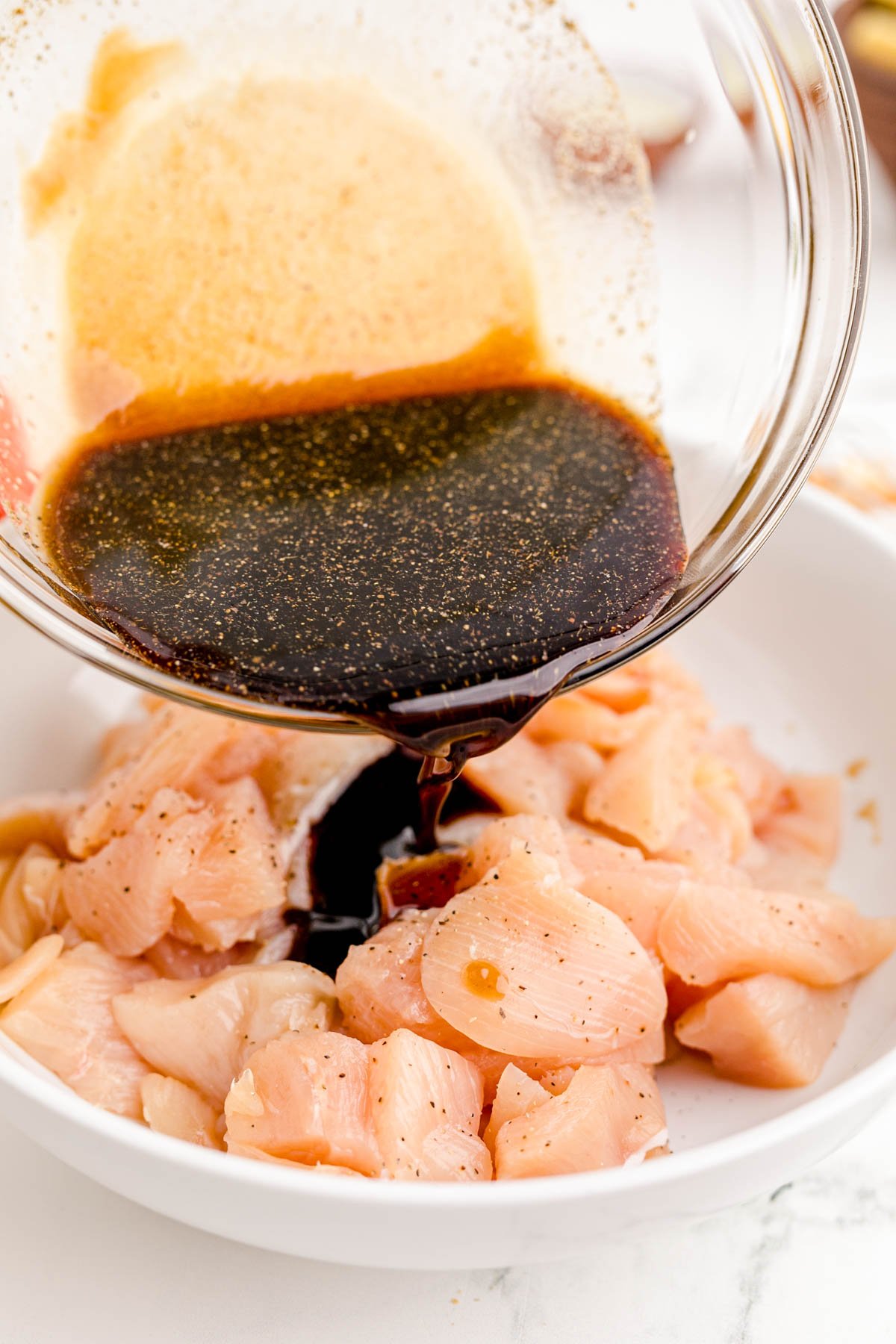 Sauce being poured over pieces of chicken in a white bowl.