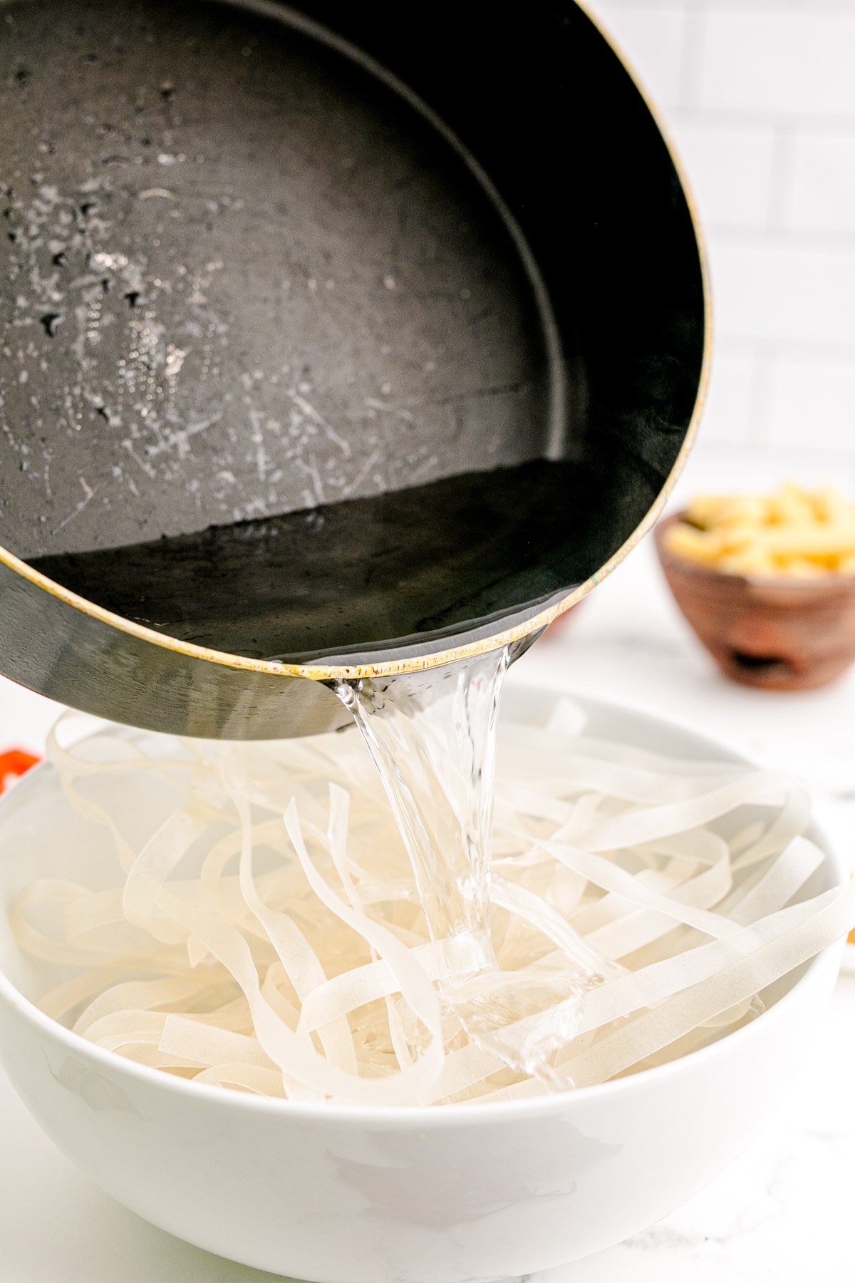 Boiling water being poured over rice noodles in a white bowl.