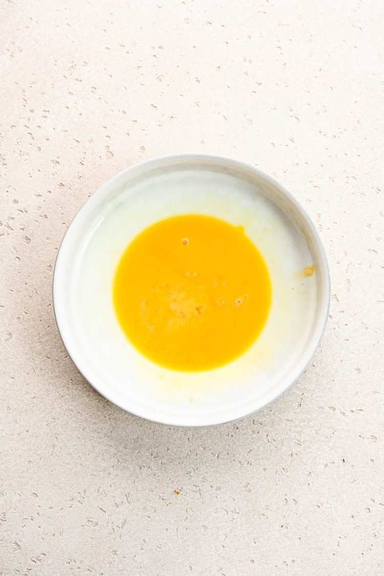 Beaten eggs in a small white bowl.