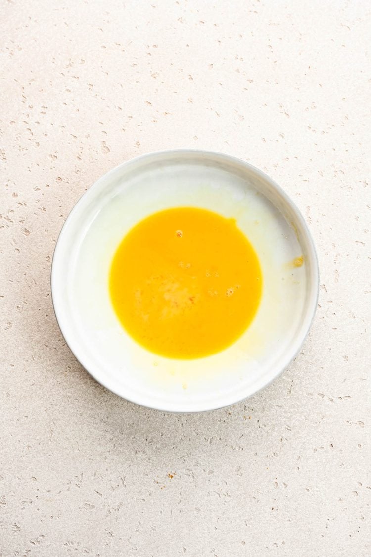 Beaten eggs in a small white bowl.