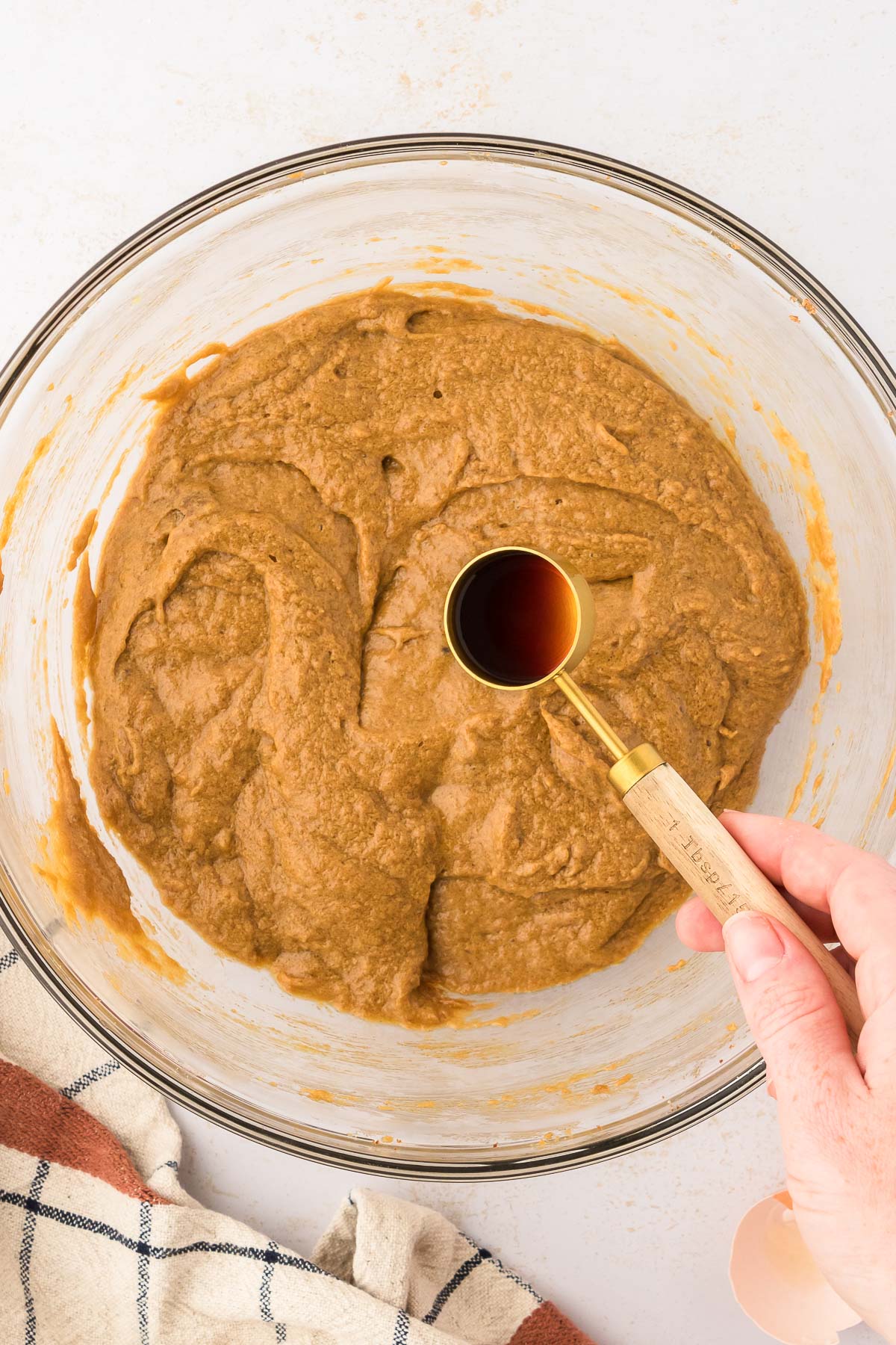 A woman's hand adding a measuring spoon of vanilla extract to a bowl with cookie dough.