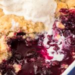 A pan filled with blueberry cobbler, vanilla ice cream melting into it.