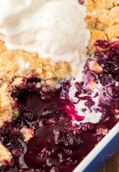 A pan filled with blueberry cobbler, vanilla ice cream melting into it.