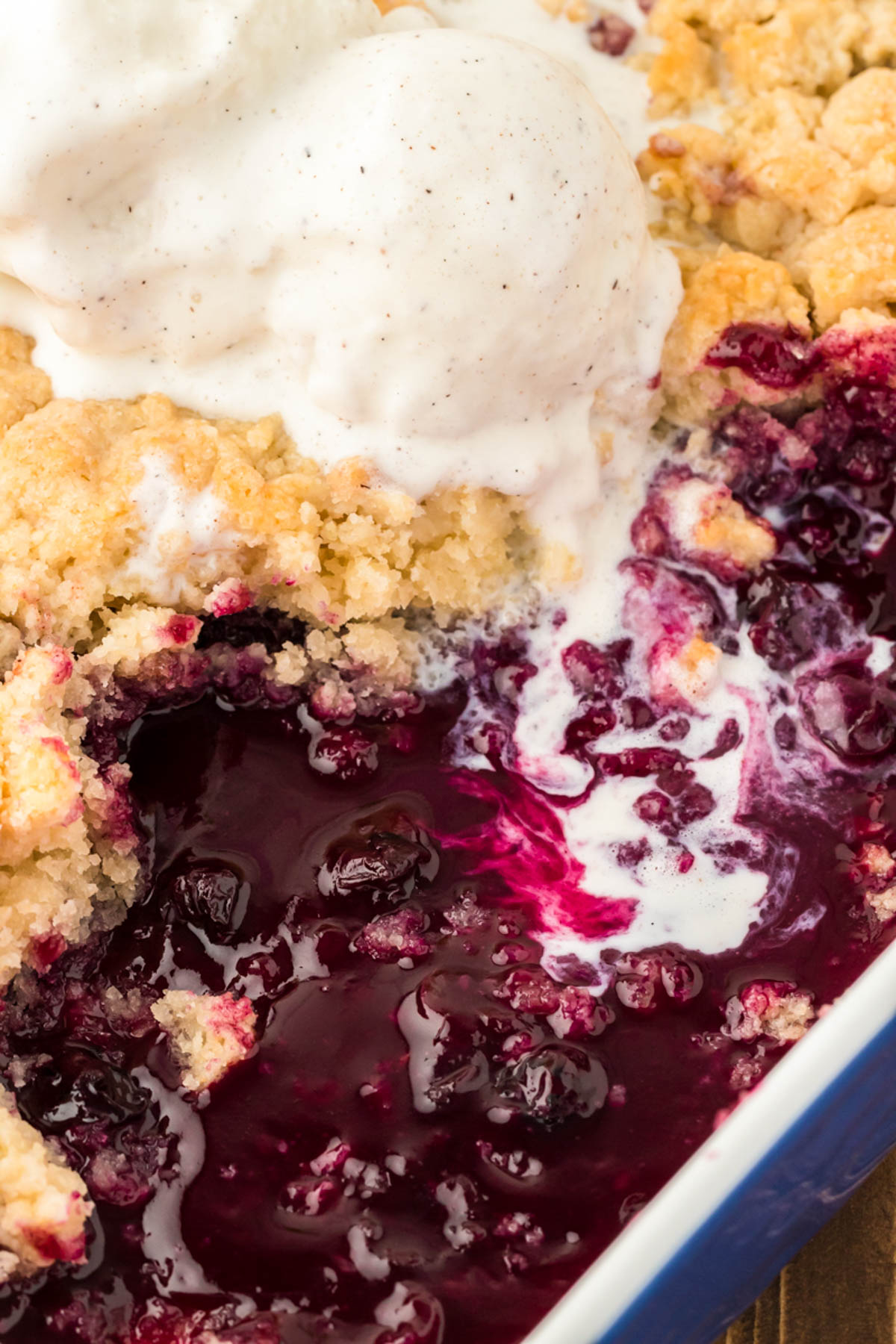 A pan filled with blueberry cobbler, vanilla ice cream melting into it.