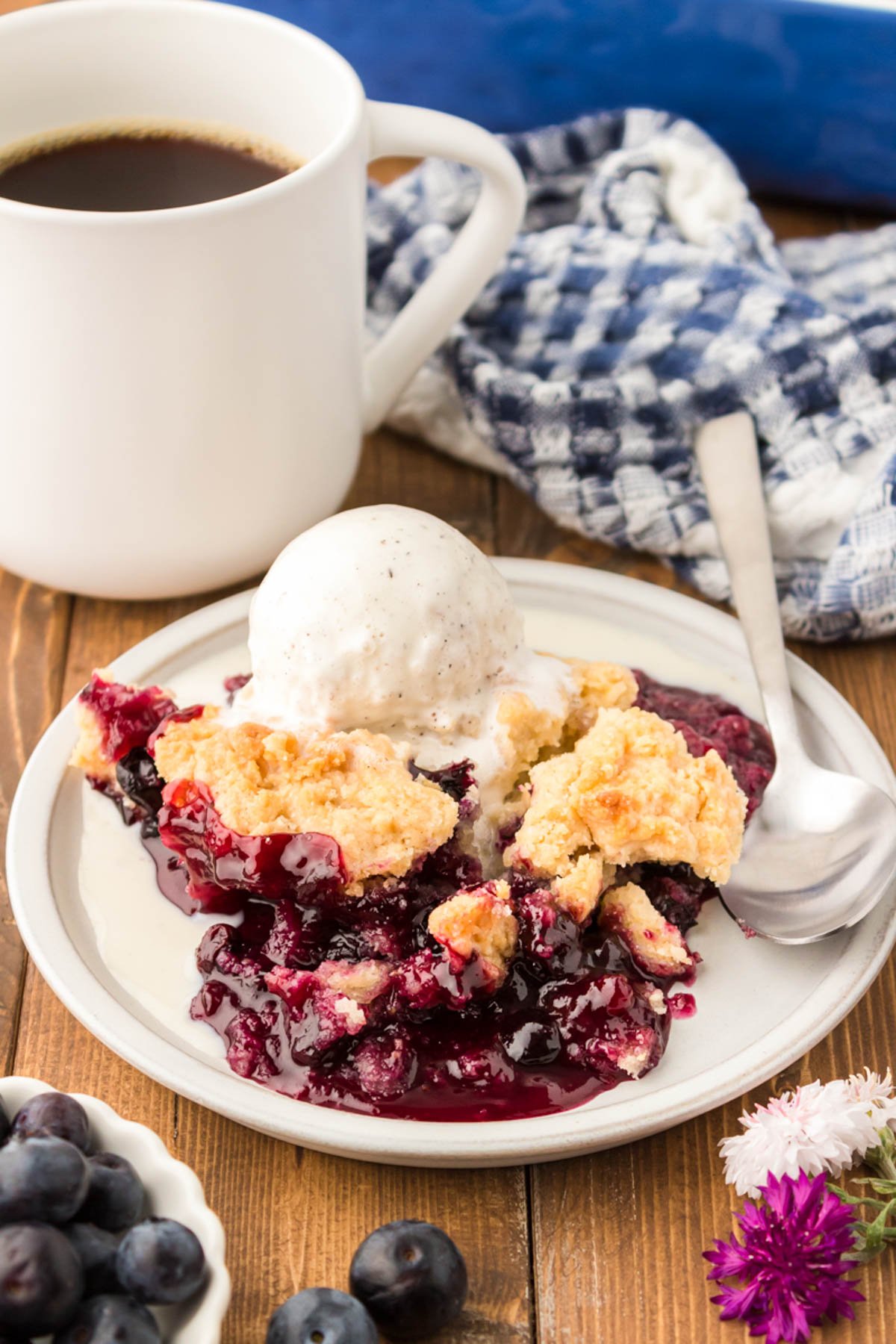 A serving of blueberry cobbler on a white plate on a wooden table. 