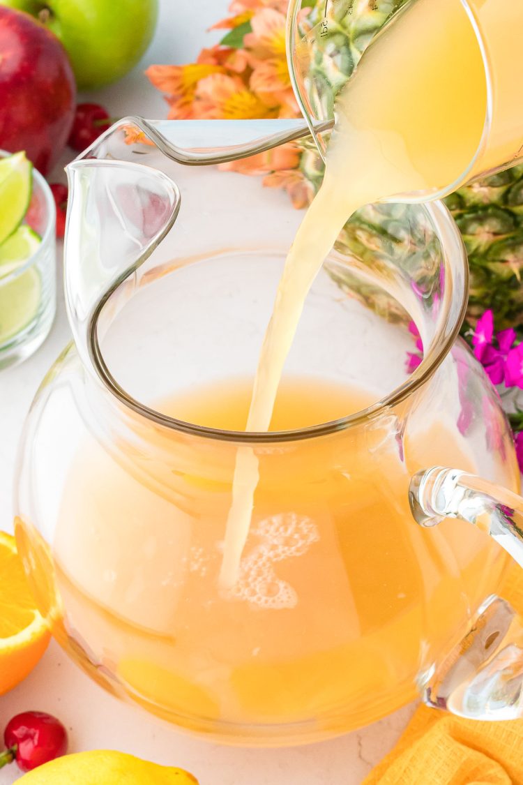 Orange, pineapple, guava juice being poured into a glass pitcher.