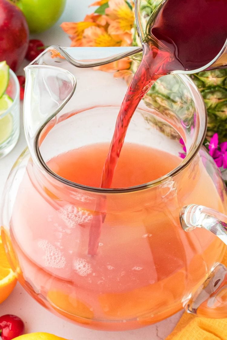 Cran-cherry juice being poured into a glass pitcher to make punch.