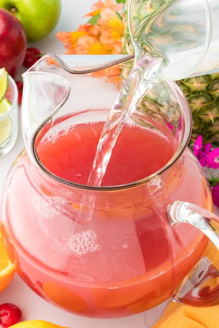 Lemon-lime soda being poured into a glass pitcher to make Hawaiian fruit punch.
