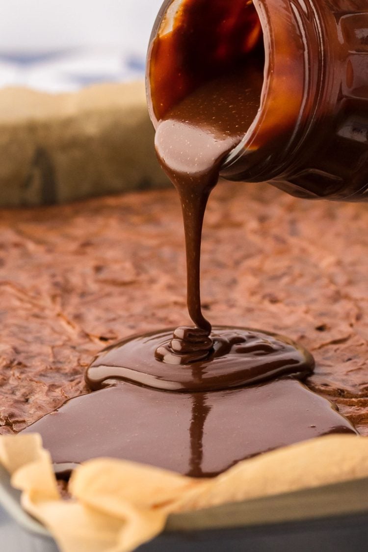 hot fudge sauce being poured on top of a pan of brownies.