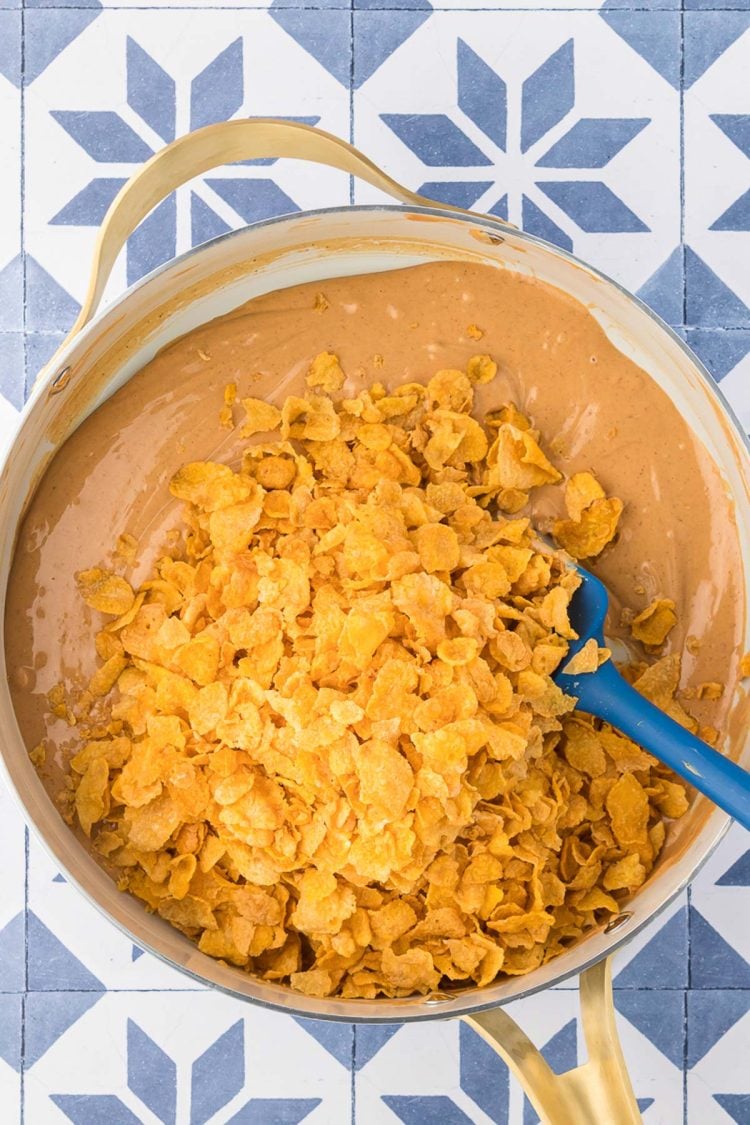 Melted peanut butter and peanut butter chips in a skillet with cornflakes being added.