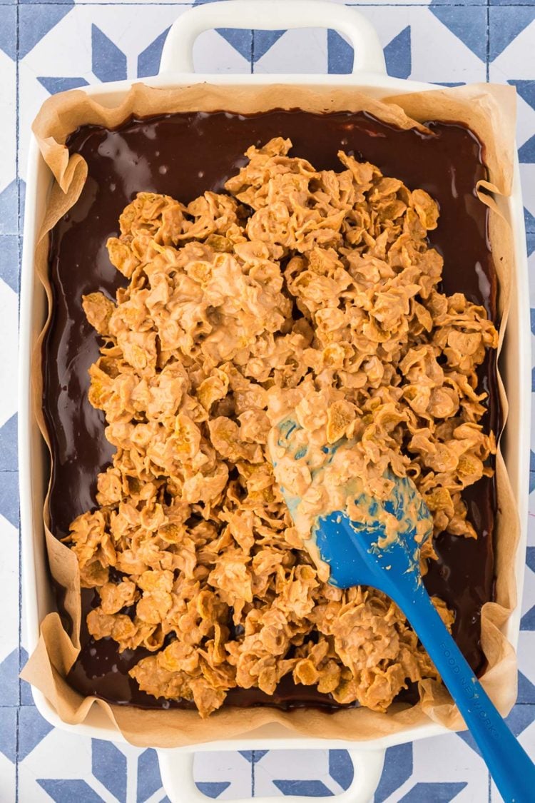 Peanut butter corn flake mixture being spread over the top of brownies.