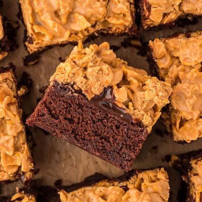 Overhead photo of peanut butter crunch brownies on parchment paper, the middle one has been turned on it's side to show the layers.