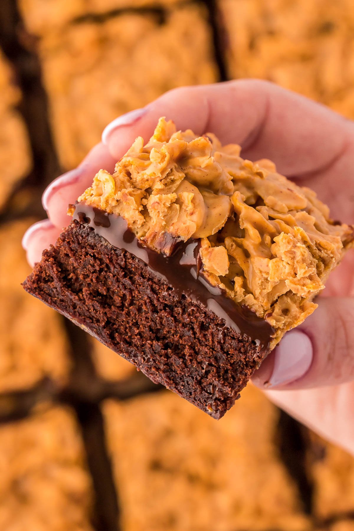 A woman's hand holding a peanut butter crunch brownie to the camera.