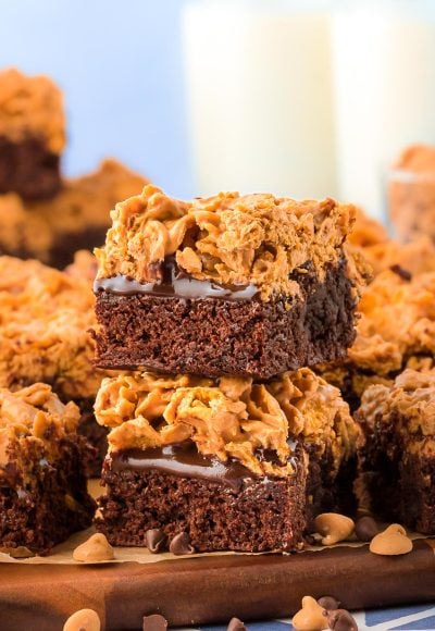 A stack of two peanut butter crunch brownies on a wooden plate with more in the background.